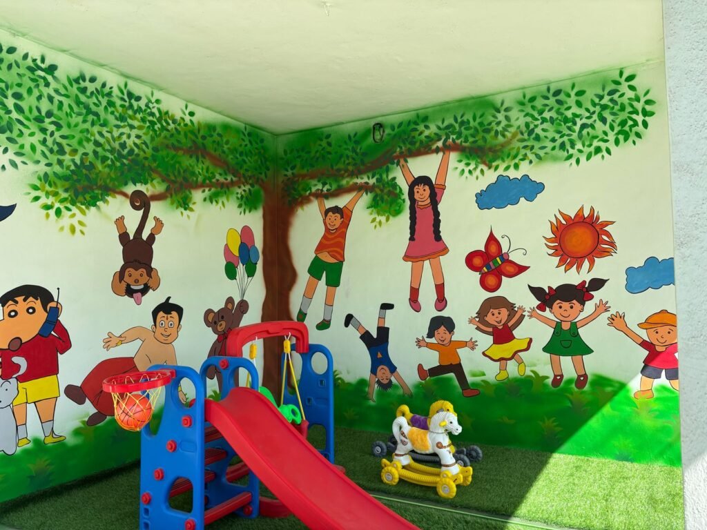 The indoor play room, its walls painted as a green tree canopy, with a small slide