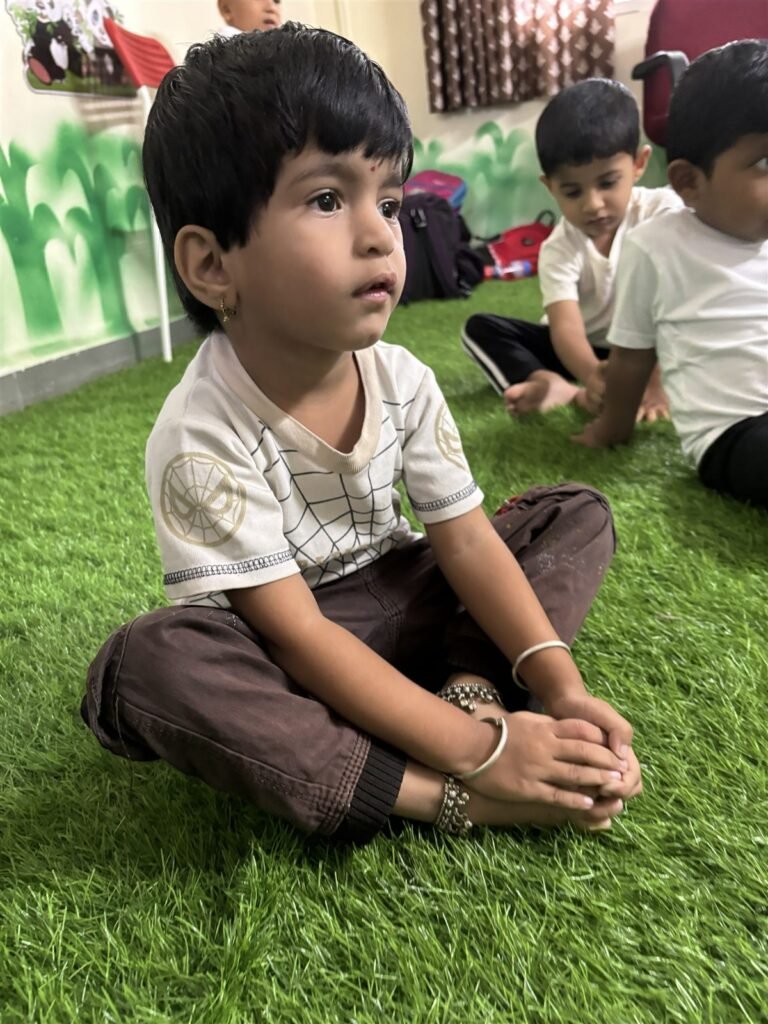 A young child sitting cross-legged and listening in a Tiny Tots classroom
